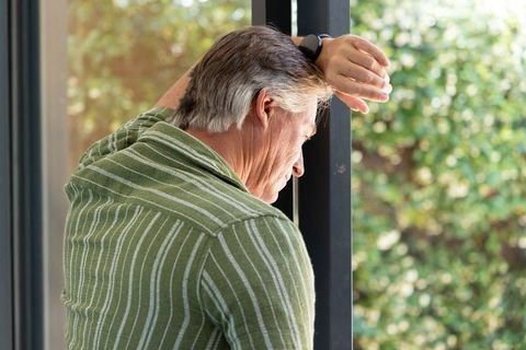 Senior man leaning on glass door frame wearing green striped sweater gazing at garden