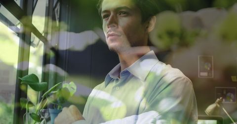 Contemplative Businessman Behind Green Foliage in Modern Office