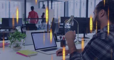 Focused professional typing on laptop in open-plan office with terrarium and notebooks