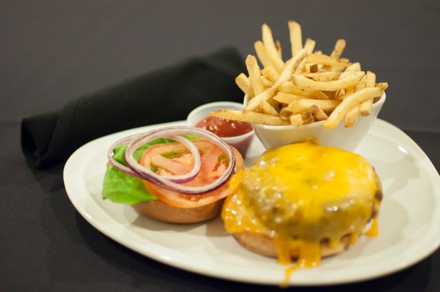Cheeseburger with melted cheese served with french fries and a side of fresh vegetables including onion slices, tomato, and lettuce. Ketchup is provided in a small dish. Ideal for restaurant menus, food blogs, culinary magazines, and advertisements focusing on American cuisine or quick meal options.