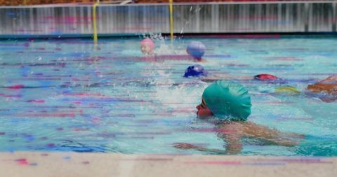Young swimmer doing freestyle breathing at outdoor pool with colorful caps and lane ropes