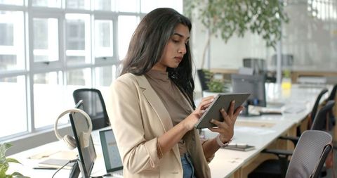 Indian woman using tablet in modern open-plan office, professional casual business style