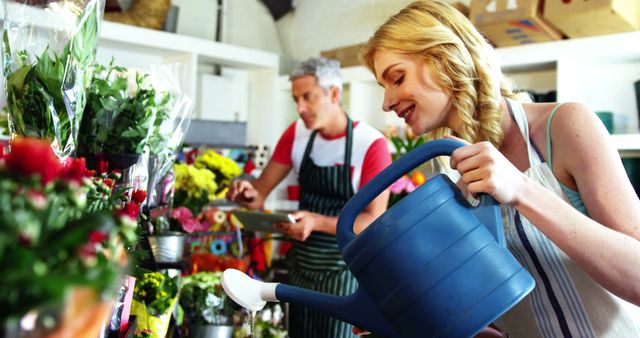 Happy Woman Watering Plants in Florist Shop with Worker in Background - Download Free Stock Images Pikwizard.com