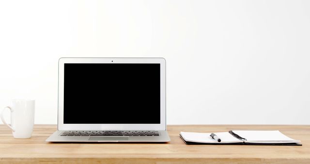 Modern minimalist workspace featuring a blank laptop screen, notebook, pen, and coffee mug on a clean wooden desk. Ideal for content related to remote work, productivity, blogging, freelancing, or study environments.