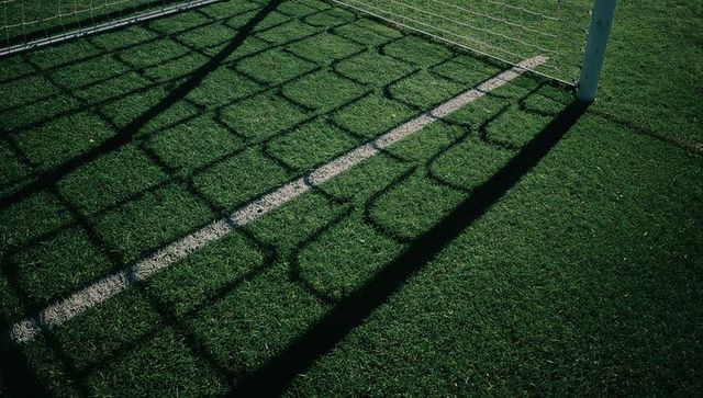 Goal net shadow casting geometric grid on artificial turf along white line and goalpost