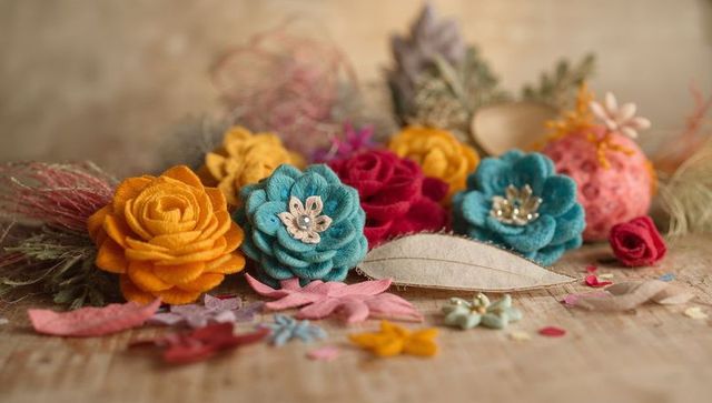 Handcrafted felt flower arrangement with beads and cut petals on rustic tan wood surface