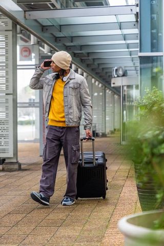 Urban traveler walking through transit canopy pulling black suitcase and talking on phone