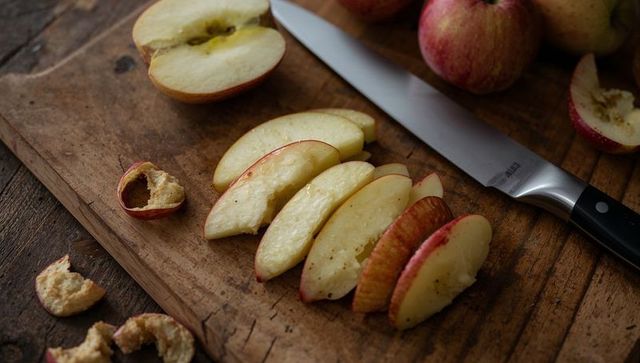 Sliced apple wedges on rustic wooden cutting board with chef knife, warm moody light