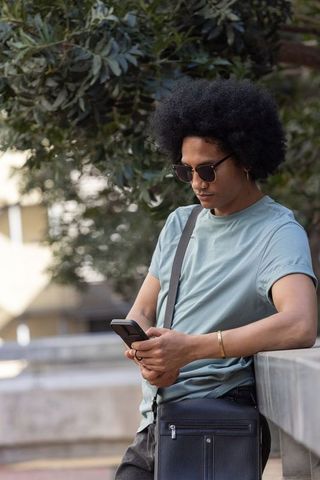 African american man using smartphone while leaning on railing under tree-lined canopy