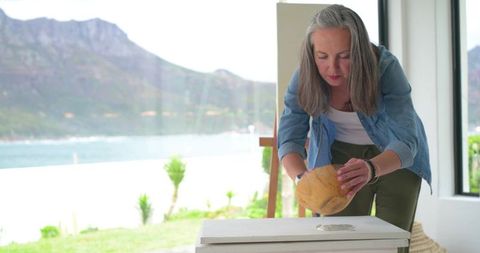 Senior woman creating pottery bowl in sunlit studio with ocean view