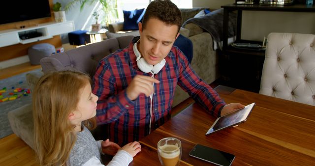 Father spends quality time with daughter while using a digital tablet at home. Casual setting suggests a relaxed family atmosphere. Can be used in articles or adverts related to parenting, technology use in families, quality time, and modern lifestyles.