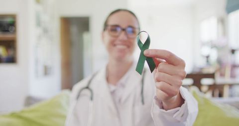 Smiling Female Doctor Holding Green Awareness Ribbon Indoors