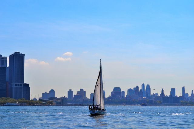 Sailboat sailing in calm waters with prominent urban skyline in background. Perfect for travel websites, maritime-themed designs, and advertisements related to sailing, boating, vacations, and urban exploration.