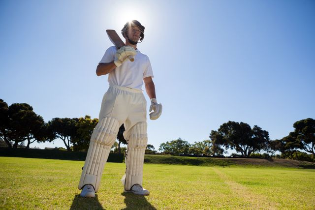 Low angle view of confident player with cricket bat standing against blue sky