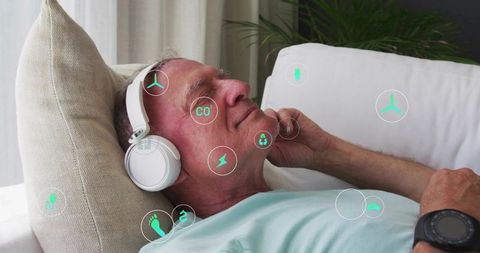 Senior man relaxing with wireless headphones on sofa displaying eco and health metrics