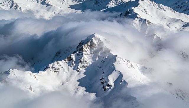 Jagged alpine peak rising through swirling clouds and snowfields in high mountain panorama
