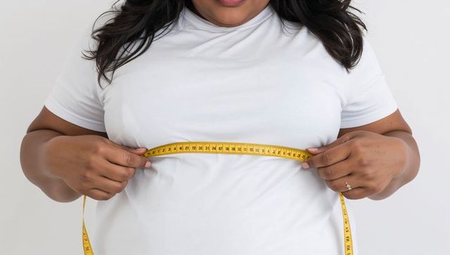 Plus-size woman measuring bust with yellow tape wearing white t-shirt closeup