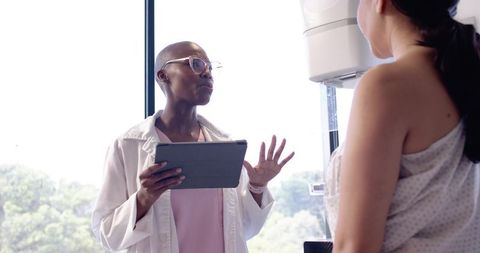 African American Clinician Consulting Hispanic Patient During Mammogram Using Tablet