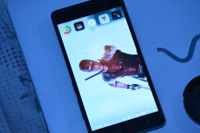 Smartphone with an action movie character set as wallpapaper displayed on the home screen. Icons for various apps including a browser and messaging are visible. Useful for marketing mobile technology, highlighting smartphone customization, or app promotion.
