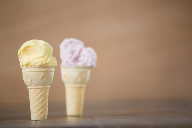 Vanilla and strawberry ice cream cones placed on a wooden surface. Ideal for use in food blogs, summer-themed promotions, dessert menus, and advertisements for ice cream parlors. The image evokes a sense of refreshment and indulgence, perfect for marketing materials aimed at highlighting sweet treats and cold desserts.