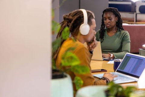 African american professionals collaborating at coworking table with laptops, headphones