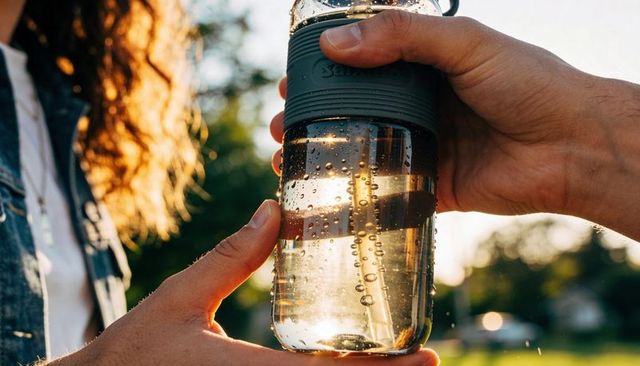 Handing reusable water bottle with silicone grip during golden hour outdoors