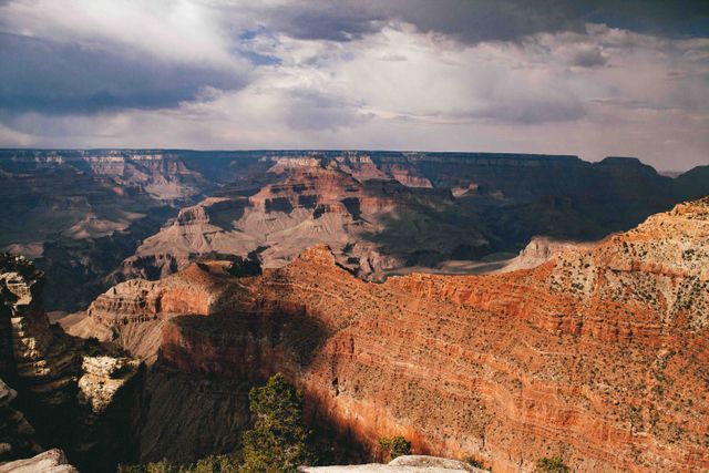Grand Canyon landscape highlighted by dramatic cloud cover, showcasing the vast cliffs and geological formations. Perfect for travel blogs, nature documentaries, educational materials, desktop wallpapers, and promotional content for tourism.