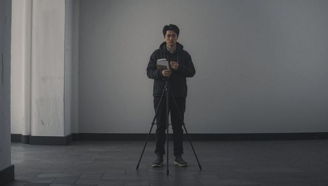 Minimalist Content Creator Standing with Tripod and Notebook in Monochrome Studio