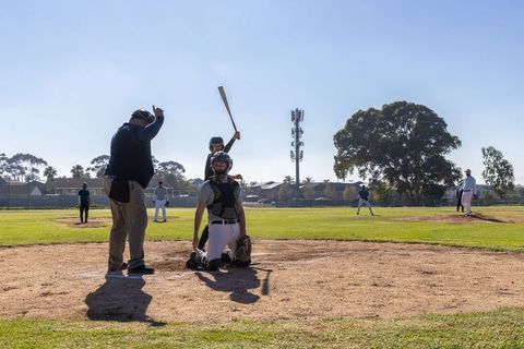 Catcher kneeling umpire signaling strike pitcher delivering pitch on sunny baseball field