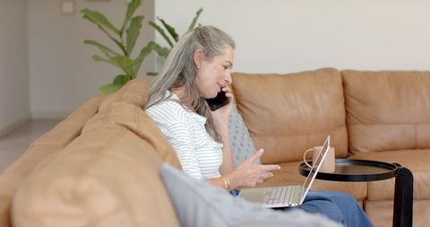 Senior Woman Multitasking with Phone and Laptop in Cozy Living Room