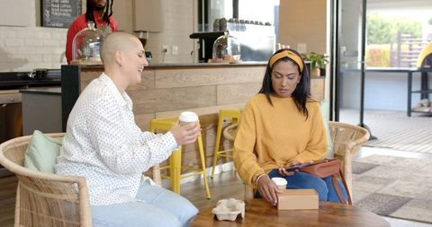Multicultural Friends Chatting Over Coffee and Pastry on Cozy Cafe Patio Holding Takeaway Box