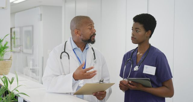 African american male and female doctors holding clipboard and tablet, talking at hospital. Medicine, healthcare, lifestyle and hospital concept.