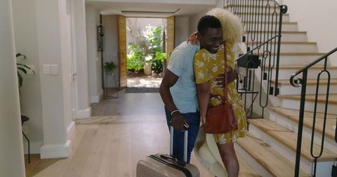 African American couple hugging in foyer with suitcase and handbag, joyful reunion