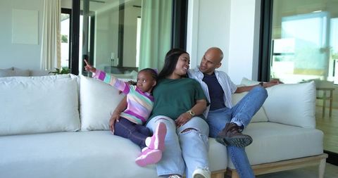 Family relaxing on modern sofa in open-plan living room, daughter pointing out window