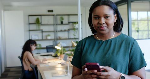African american professional woman holding phone in modern collaborative office space