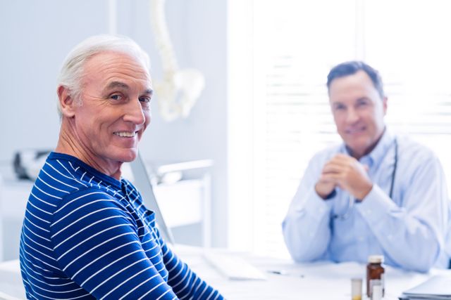 Portrait of senior patient smiling in clinic with doctor in background