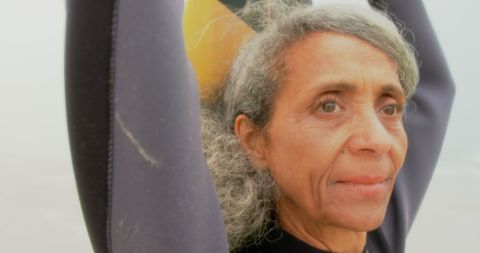 Thoughtful Senior Woman Holding Surfboard at Beach