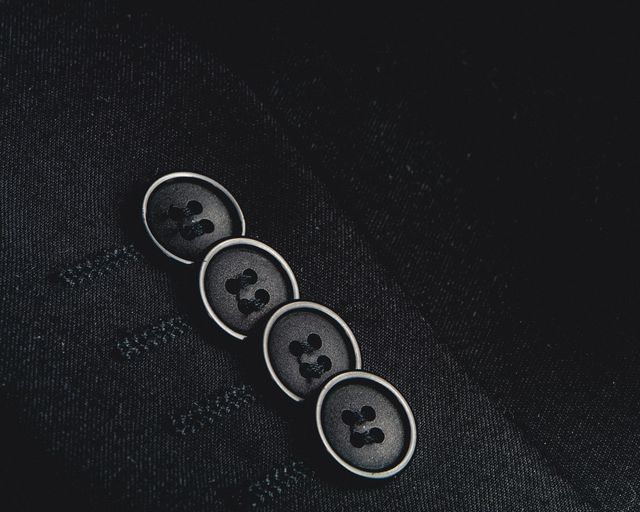 High-detail image of black suit buttons against dark fabric background. Ideal for fashion industry material, tailoring blogs, and articles on formalwear. Can be used in advertisements for tailoring services, magazines, and professional portfolio displays.
