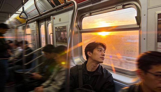 Asian commuter watching golden sunset through subway window with lens flare and reflection