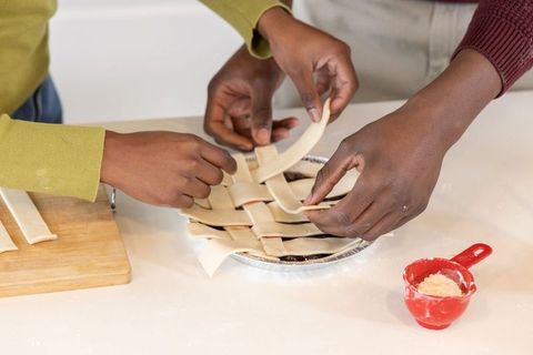 African american friends weaving lattice pie crust on countertop, teamwork baking closeup