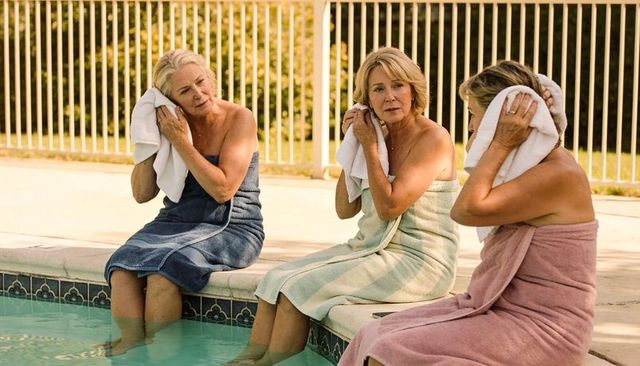 Three senior women relaxing by poolside, drying hair with towels, summer wellness