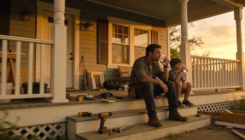 Father and son taking break during porch renovation at golden hour, drinking water