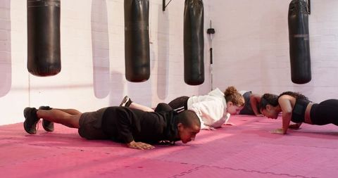 Female coach guiding group through plank push-ups on red mats under punching bags