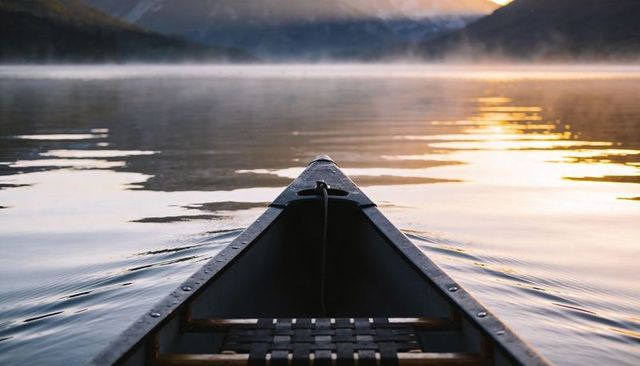 Canoe bow gliding on misty sunrise lake with golden reflection and tranquil wilderness