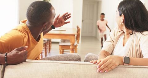 Parents calling child running down hallway toward couch in bright natural light home