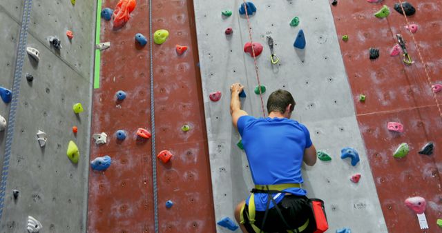 Man climbing colorful indoor wall in a recreational and fitness setting, showing focus and determination. This stock photo is ideal for promoting active lifestyle, health and fitness programs, adventure activities, gym facilities, and sports-related events.