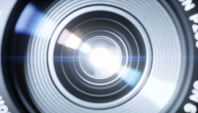 Macro camera lens front element with visible aperture blades and dramatic lens flare