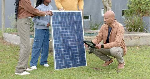 Diverse family installing solar panel in backyard while checking tablet connections
