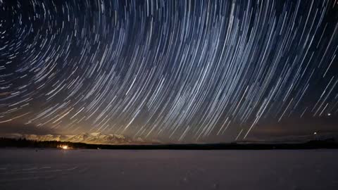 Timelapse Video Capturing Wide Star Trails Rotating Over Snowy Lake and Mountain Horizon