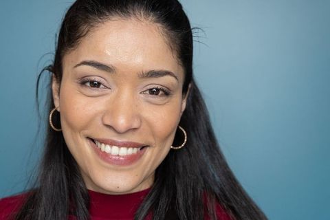 Smiling woman in maroon top wearing gold hoop earrings against teal-blue backdrop headshot